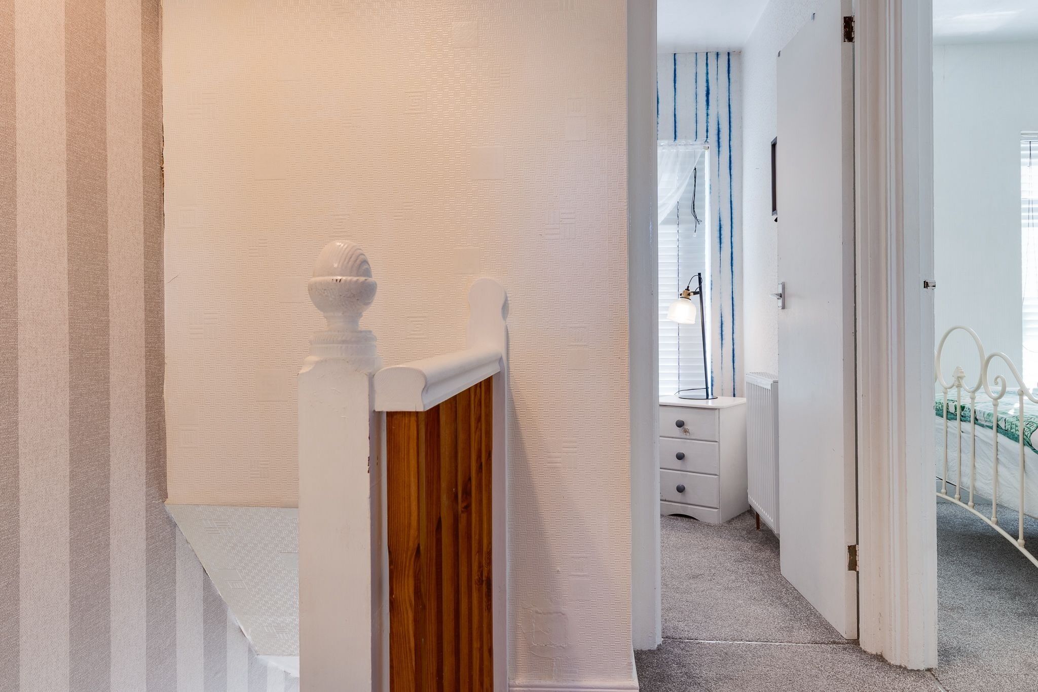 Un couloir avec une porte blanche donnant sur une pièce équipée d’un radiateur et d’une fenêtre avec des stores.