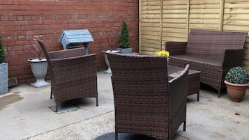 A patio area with wicker furniture, a brick wall, and a wooden gate.