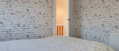 A bedroom with a brick-patterned wall, a bed with a floral bedspread, and a door leading to another room.
