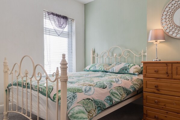 Un dormitorio con cama, cómoda, ventana con persianas y espejo adosado a la pared.