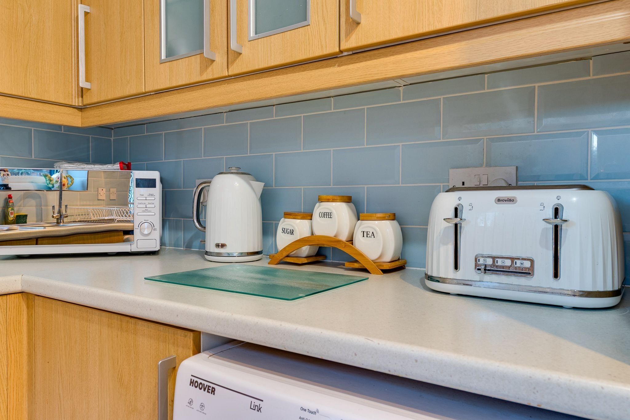 A kitchen with wooden cabinets, a microwave, a coffee maker, a toaster, and a vacuum cleaner.