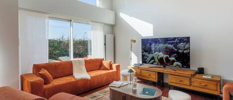 Ein modernes Wohnzimmer mit einem großen Fernseher, orangefarbenen Möbeln und einem Streifen Teppich.
