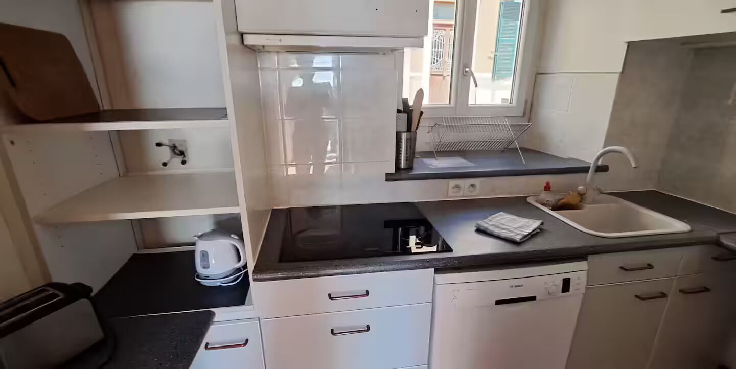 A compact kitchen with a black countertop, white cabinets, a window, and a dish rack.