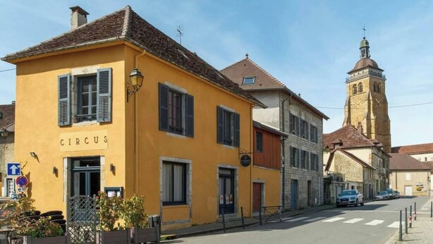 A yellow building with a sign reading "CIRCUS" on the ground floor, adjacent to a church with a bell tower. - CHEZ INES A place to live in Arbois - 2 to 10 pers ARBOIS (Arbois)