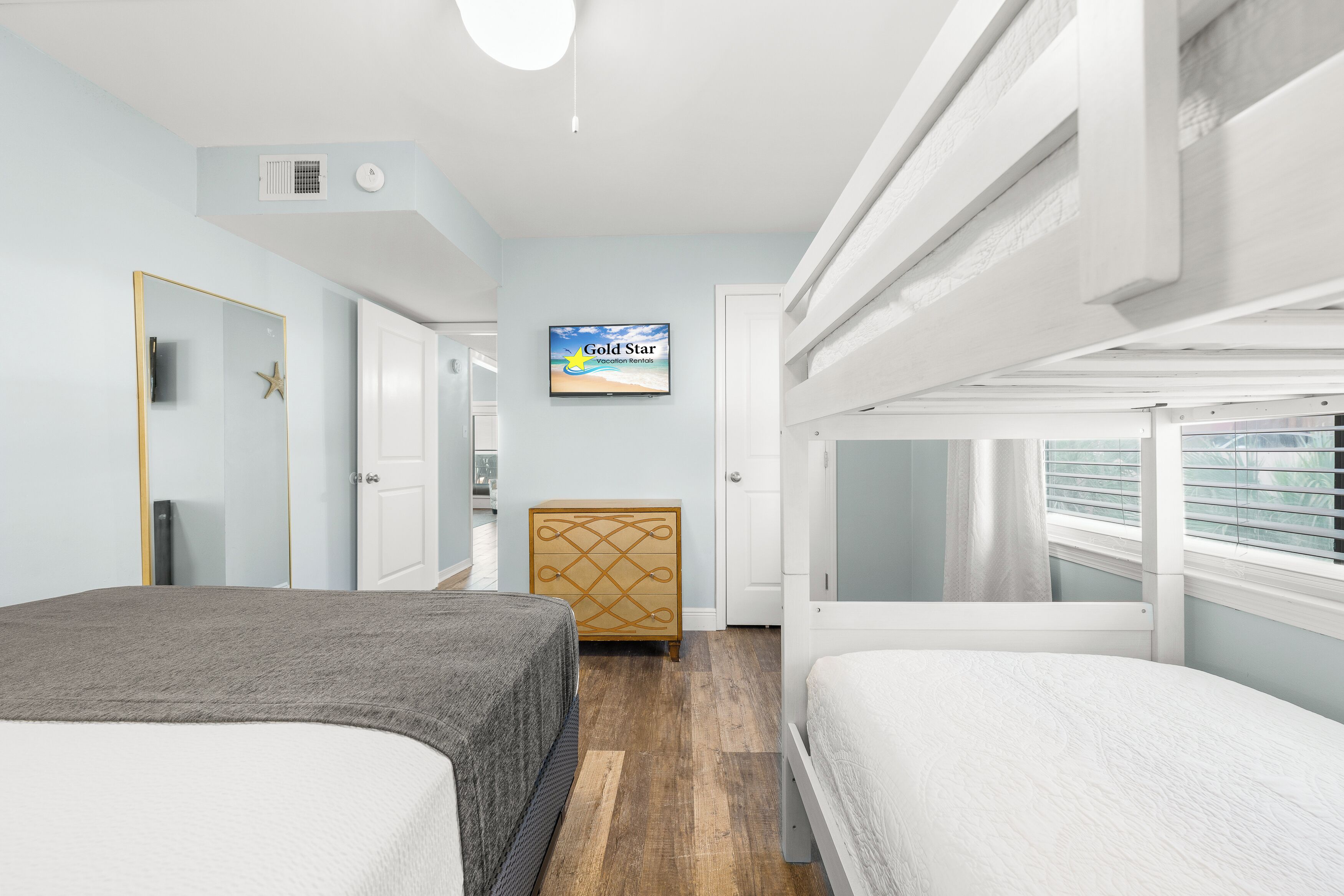 A hotel room with bunk beds, a TV on the wall, a dresser, and a starfish decoration.