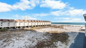 Un hotel frente a la playa con una hilera de habitaciones que dan al océano, un estacionamiento y una playa de arena.