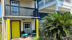 Um edifício de dois andares com uma porta amarelo-vivo e uma varanda com guarda-corrimão preto.