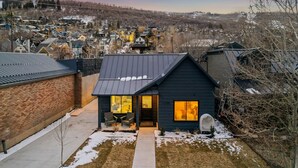 Une maison moderne à l’extérieur sombre, dotée d’une cuisine ouverte et d’un petit patio avec coin salon extérieur.