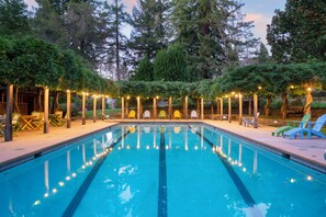 Ein Schwimmbecken mit Fliesen umgeben, mit Adirondack-Stühlen und Lichterketten.