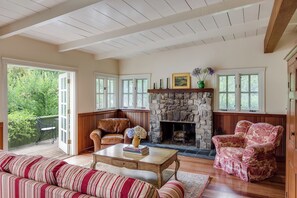 A cozy living room with a stone fireplace, wooden furniture, and large windows. - Wild Iris Retreat- Family Friendly Anderson Valley Estate with Pool, Sleeps 15 (Philo)