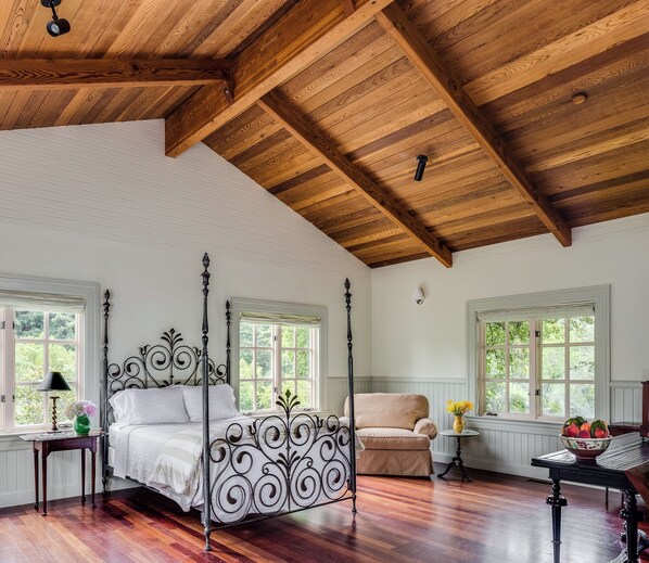 Ein geräumiges Schlafzimmer mit einem Himmelbett, Holzbalken an der Decke und großen Fenstern.