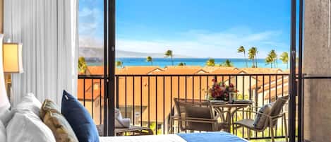 Et hotelværelse med balkon, seng, bord med stole og udsigt til stranden.