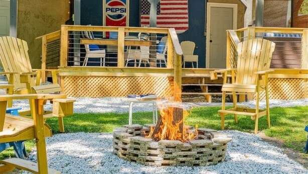 An outdoor seating area with Adirondack chairs, a fire pit, a covered patio with a Pepsi sign, and an American flag. - Explore Mayberry: 2 King Masters, 3 Bed / 3 Bath, Fire Pit (Mount Airy)