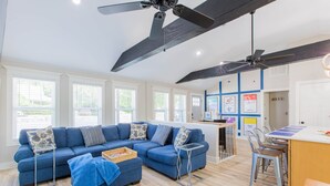 A modern living room with a blue sofa, a small table, and a kitchen area with a bar. - Explore Mayberry: 2 King Masters, 3 Bed / 3 Bath, Fire Pit (Mount Airy)