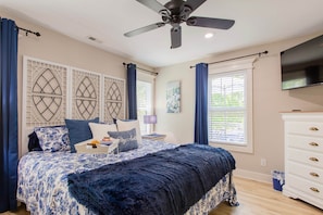 A bedroom with a bed, a ceiling fan, a TV, and a window with curtains.