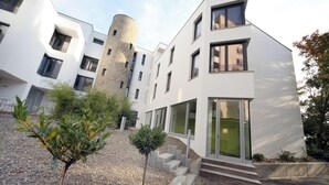 A modern building with a cylindrical tower, multiple windows, and a gravel pathway with small trees. - Conference Partner Ullrich (Elfershausen)