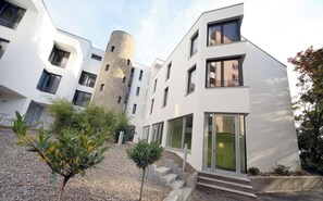A modern building with a cylindrical tower, multiple windows, and a gravel pathway with small trees. - Conference Partner Ullrich (Elfershausen)