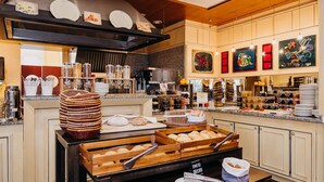 En buffet med forskellige retter, herunder brød og kager, samt en kaffestation med flere kaffemaskiner.
