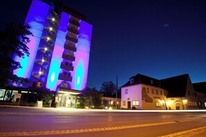 A modern hotel with a prominent vertical structure featuring illuminated windows and balconies. - Conference Partner Ullrich (Elfershausen)