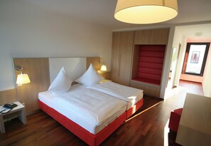 A hotel room with a large bed, two bedside lamps, a wooden headboard, and a red accent wall. - Conference Partner Ullrich (Elfershausen)