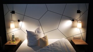 A modern hotel room with a geometric-patterned headboard, two bedside tables with lamps, and a neatly made bed with pillows. - Conference Partner Ullrich (Elfershausen)