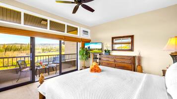 A bedroom with a large bed, a ceiling fan, a TV, a dresser, and a balcony with a view.