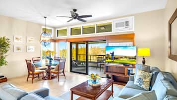 A spacious living area with a large sofa, a dining table with chairs, a television, and a ceiling fan.