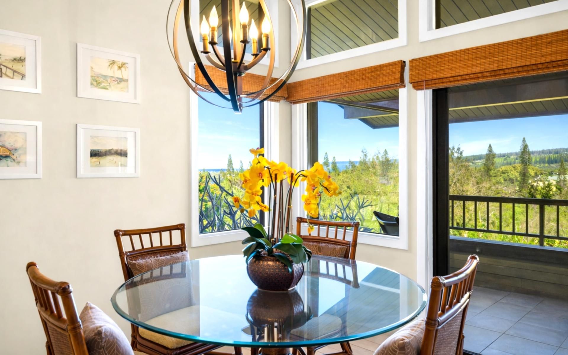 A round glass table with chairs, a vase with yellow flowers, and framed pictures on the wall.