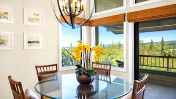A round glass table with chairs, a vase with yellow flowers, and framed pictures on the wall.