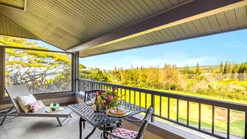 A balcony with a table, chairs, and a view of a golf course.