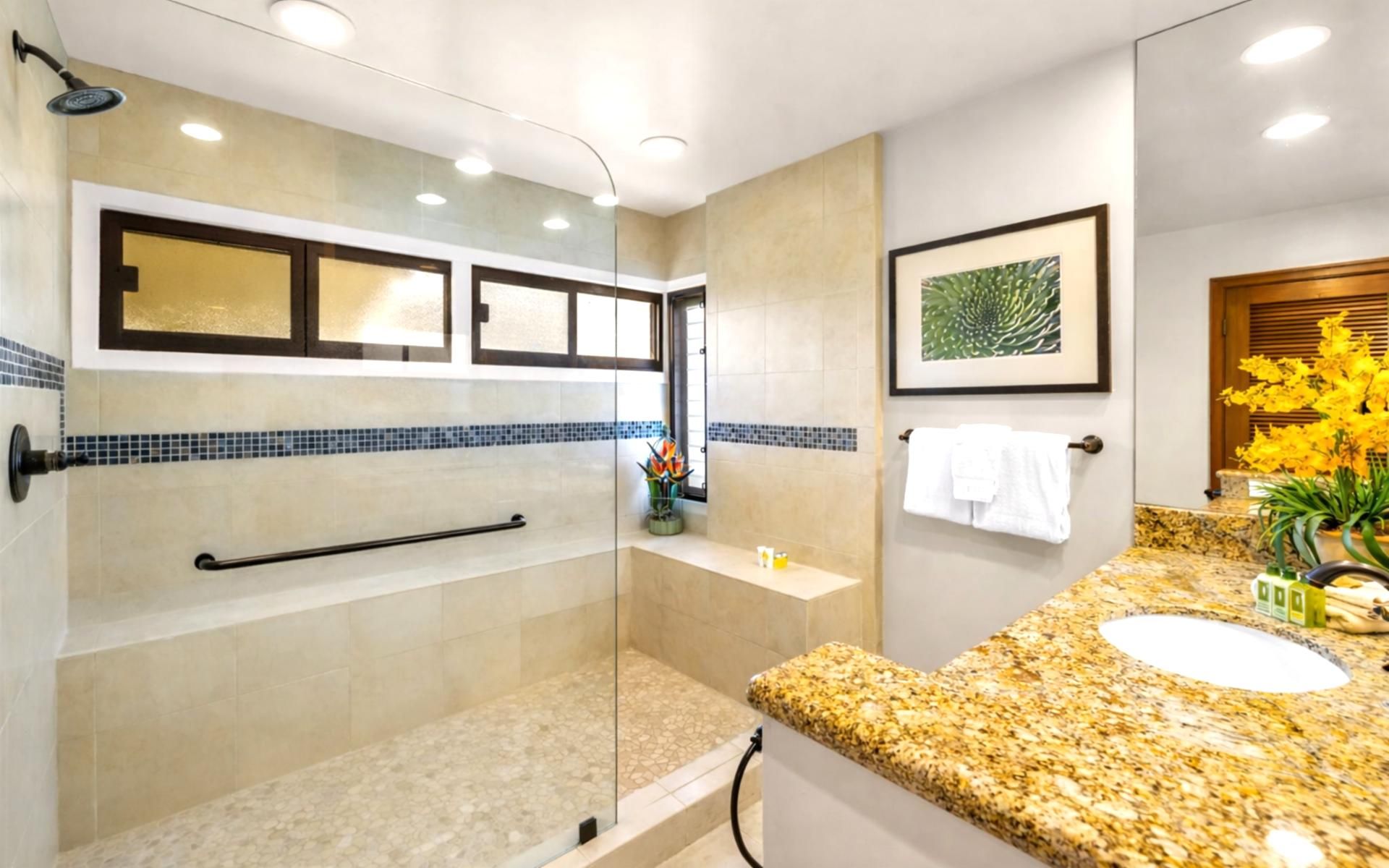 Une salle de bain moderne dotée d’une douche à parois de verre, d’un comptoir en granit, d’un lavabo et d’une œuvre d’art encadrée accrochée au mur.