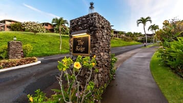 A stone sign with "The Ridge" written on it, surrounded by greenery and a paved path.