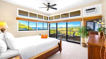 A bedroom with a large bed, a ceiling fan, a view of the outdoors, and a balcony with chairs.