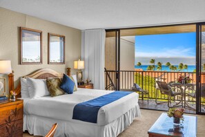 Een hotelkamer met een bed, nachtkastjes, een balkon met uitzicht op de oceaan en palmbomen.