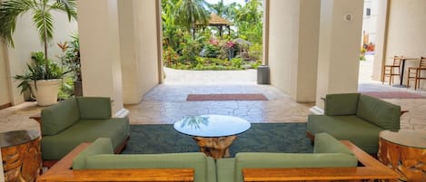 Eine Lobby mit grünen Sofas, einem zentralen Couchtisch und Blick auf einen tropischen Garten.