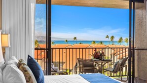 Ett hotellrum med en säng, utsikt över stranden och en balkong med ett bord och stolar.