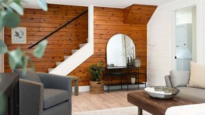 Ein modernes Wohnzimmer mit einer Holztreppe, einem Sofa, einem Couchtisch und einem dekorativen Spiegel.