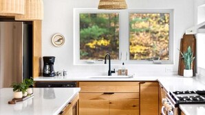 Eine moderne Küche mit Holzschränken, einer weißen Arbeitsplatte, einem schwarzen Wasserhahn und einem Fenster mit Blick auf Herbstlaub.