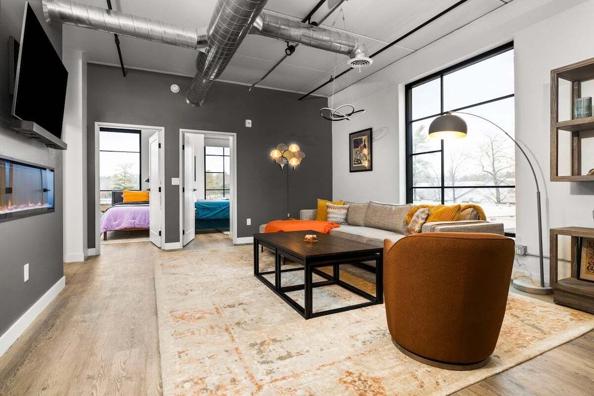 Un salon moderne avec un canapé, une table basse et une cheminée. Il y a deux portes qui donnent sur d’autres pièces, et une grande fenêtre qui laisse entrer la lumière naturelle.
