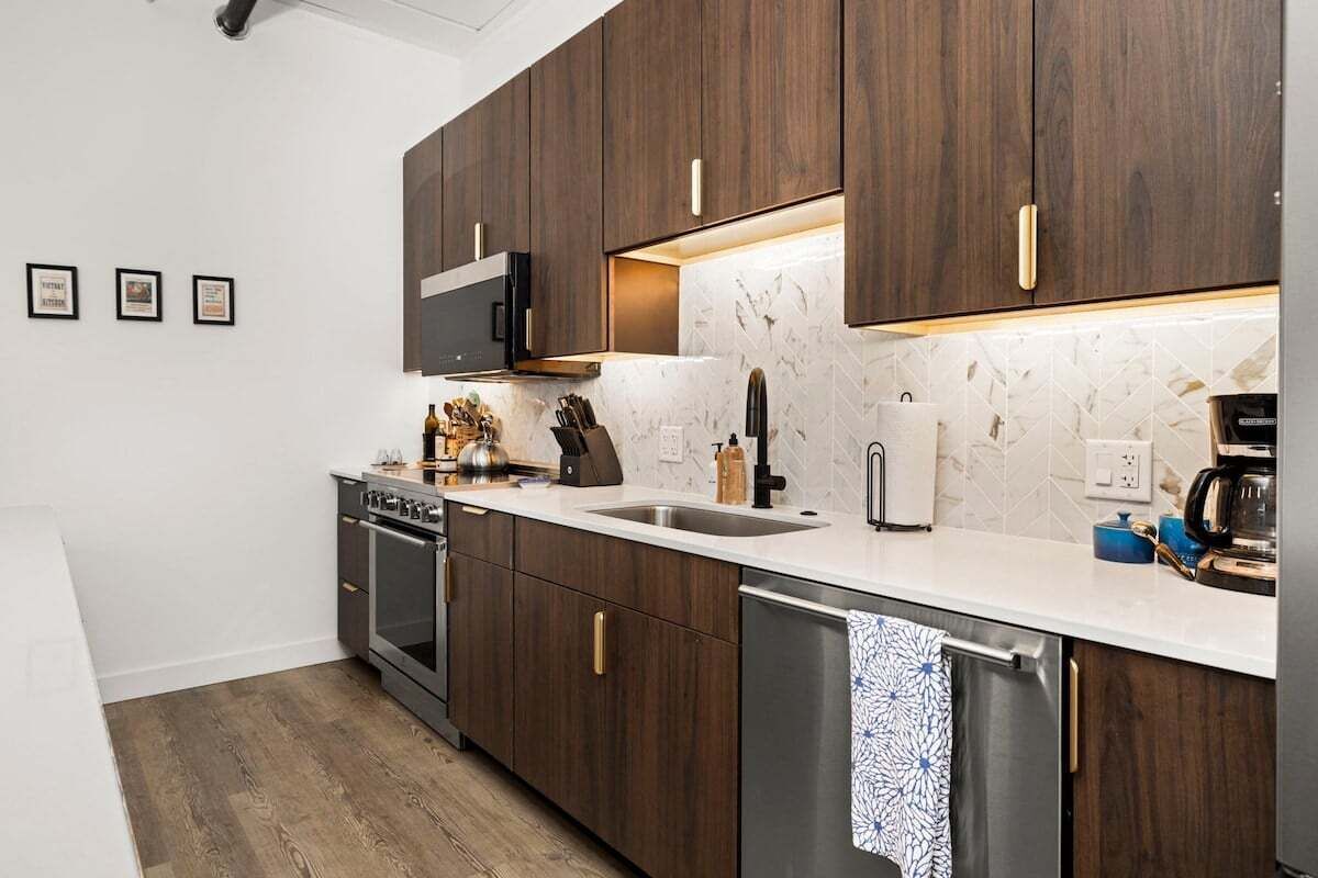 Une cuisine moderne avec des meubles en bois foncé, des appareils électroménagers en acier inoxydable et un pare-feu en marbre blanc.