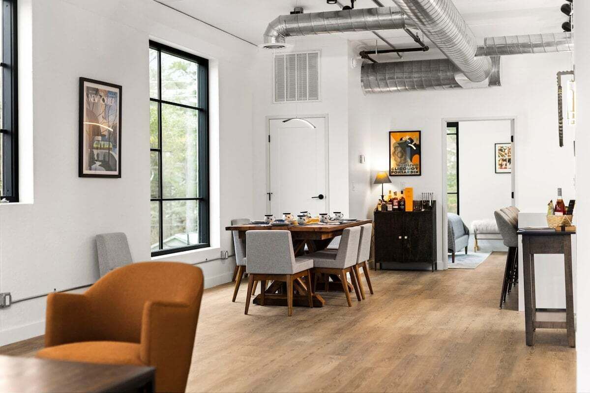 Un espace de salle à manger moderne, avec une table et des chaises en bois, un meuble noir et une fenêtre donnant sur un paysage verdoyant.