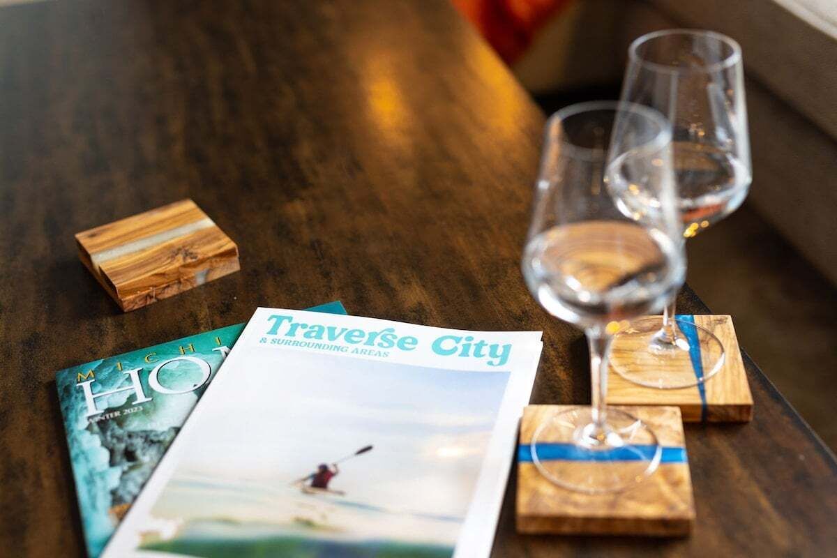 Puinen pöytä, jonka päällä on lehti nimeltä ”Traverse City” ja kaksi lasillista viiniä puisilla aluslautasilla.