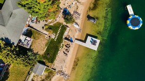 An aerial view of a lakeside property with a swimming area, a dock, and a small building with a patio. - Beach House - Lakefront with a Hot Tub! (Traverse City)