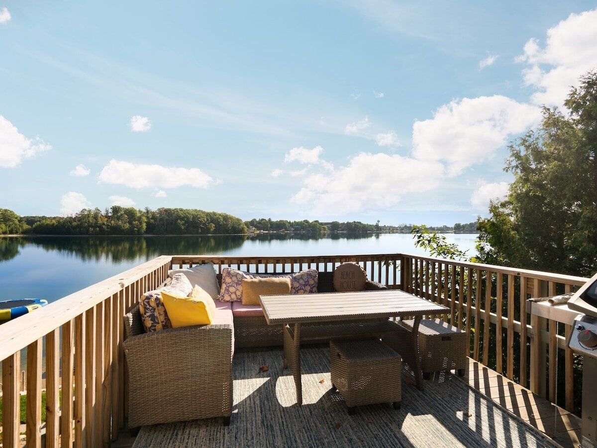 Une terrasse en bois, dotée de mobilier d’extérieur, d’un barbecue et offrant une vue sur un lac.