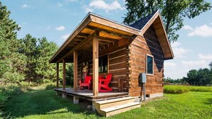 A log cabin with a porch, red chairs, and a small outdoor area.