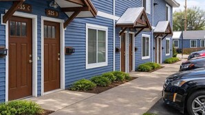 A row of blue houses with numbered doors, a parking area, and a black car parked in front. - TC Parkside H: Charming 2BR Retreat (Traverse City)