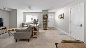 A modern living room with a sofa, coffee table, TV, and a bookshelf. - TC Parkside H: Charming 2BR Retreat (Traverse City)