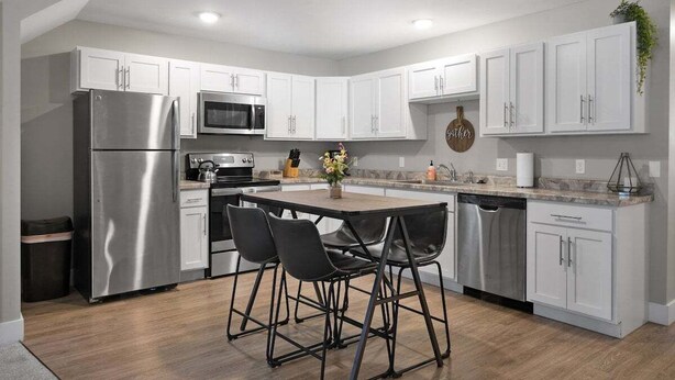 A modern kitchen with white cabinets, stainless steel appliances, and black bar stools. - TC Parkside H: Charming 2BR Retreat (Traverse City)
