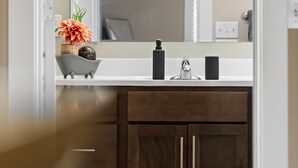 Un bagno con un mobile vanitario in legno scuro, un lavandino bianco e uno specchio con tre luci.