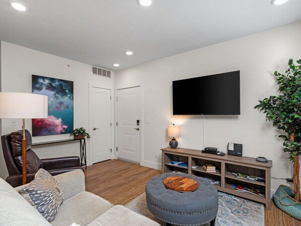 A living room with a sofa, ottoman, TV, and a plant.